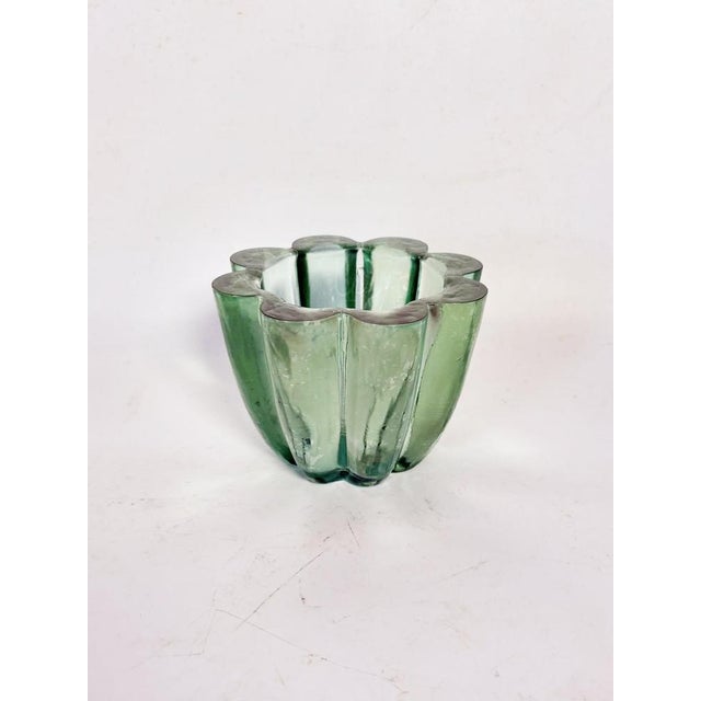 A 1940s Art Deco ashtray crafted from thick molded glass in a nuanced green hue. Its circular form is punctuated by...