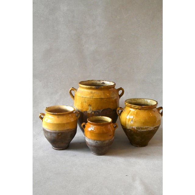 An antique French confit jar in glazed earthenware, dipped halfway in a warm ochre glaze over a bare terracotta base, with...