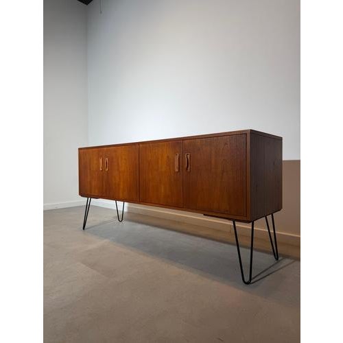 A striking mid-century modern G-Plan sideboard, crafted in beautifully figured teak and elevated on elegant black hairpin...