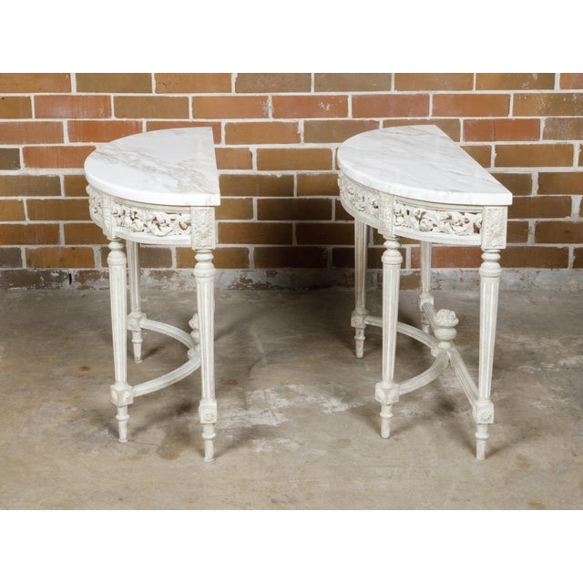 A pair of French Louis XVI style demi-lune console tables from the 19th century with white veined marble tops, carved...