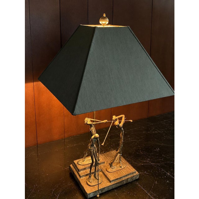 A vintage Frederick Cooper table lamp featuring three elongated golfers arranged across a stepped base, each captured at a...
