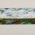 This Framed Signed J. Akston "Exuberance of Spring, 1974" Artwork captures a vivid horizontal landscape rendered in...