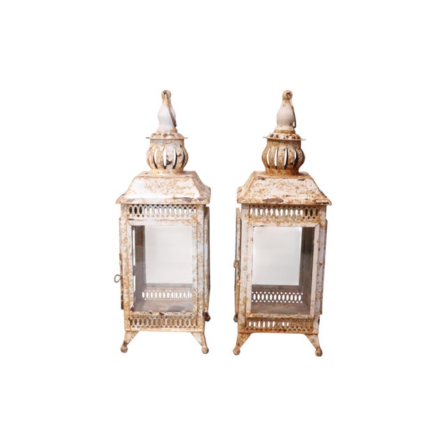 A pair of rustic pagoda shaped lanterns. The metal frame has four side ribs that support glass panels with reticulated...