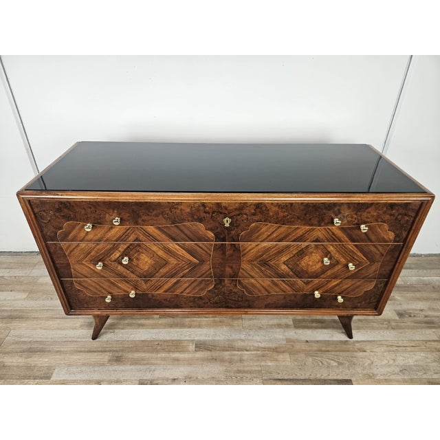 A 1950s Art Deco chest of drawers entirely clad in burl, with maple trim along the three large drawers and a black glass...
