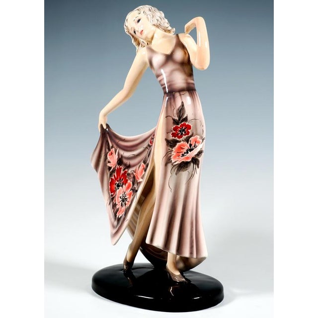 A graceful young dancer in a long, low-cut, high-slit pale pink dress with an extensive floral pattern, her head tilted to...