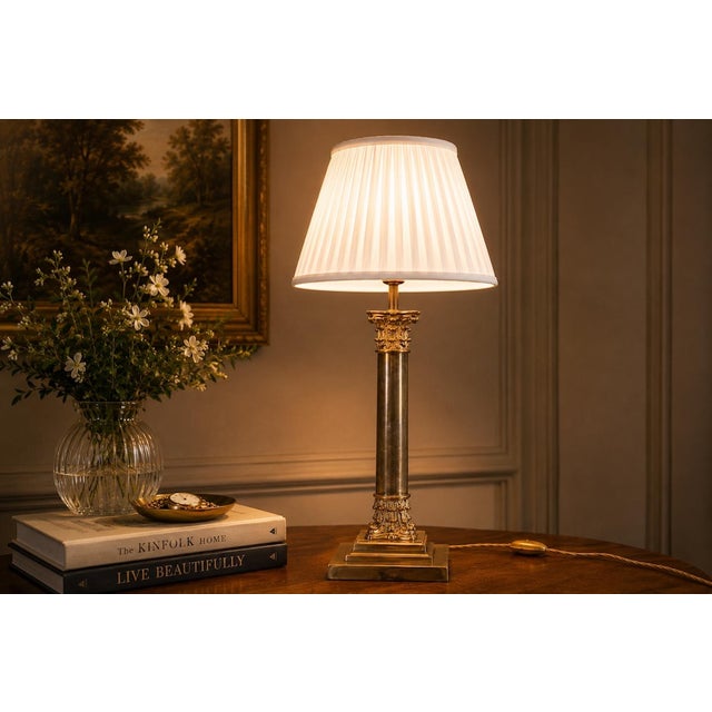 A refined and elegant brass table lamp inspired by classical architectural forms, featuring a tall cylindrical column with...