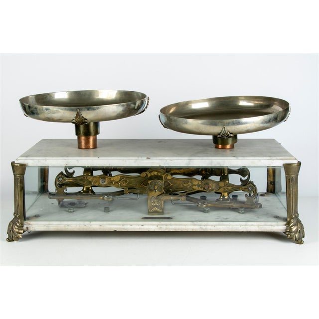 An antique French balance scale by Rafael M. Volpi with brass pans and an ornately engraved mechanism visible through...