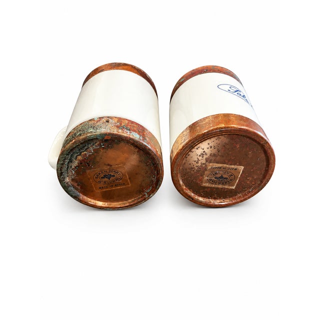 Charming 1970s vintage salt and pepper shakers featuring white ceramic handled bodies, blue lettering, and perforated...