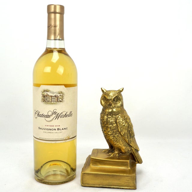 A heavy, glittering brass bookend featuring a scholarly owl perched atop a stack of books, with the bottom volume titled...