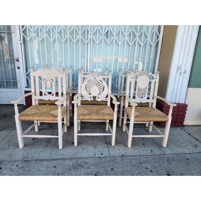 Hand-carved wooden armchairs with a distressed white and pastel iridescent finish. Each chair has a woven rush seat and...