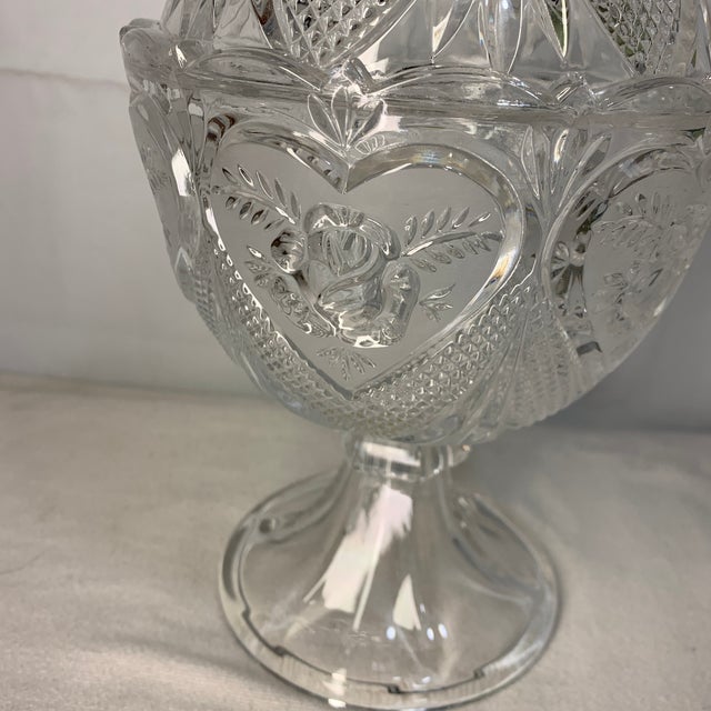 This vintage pressed clear crystal glass footed candy dish features a repeating heart and rose pattern with a matching...
