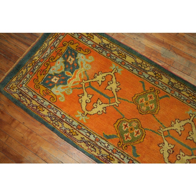 An early 20th century antique Oushak runner featuring a pumpkin orange field, forest green border with an all-over design...