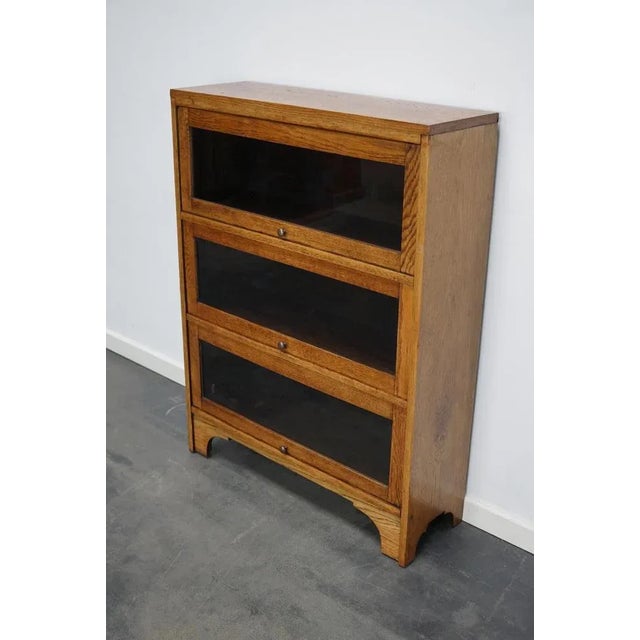 This bookcase was produced in Germany around the 1930s. It features 3 compartments with glass sliding doors. The interior...