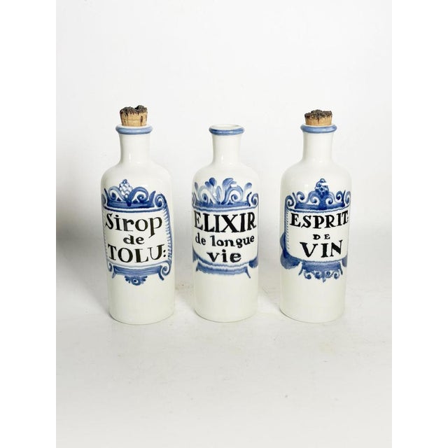 Set of three decorative ceramic bottles inspired by traditional apothecary jars. Each bottle features an inscription...