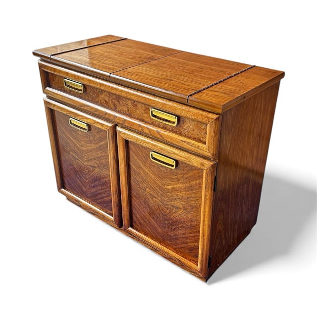 A stunning vintage Broyhill bar cabinet featuring gorgeous bookmatched walnut veneer, original brass recessed pulls, and a...