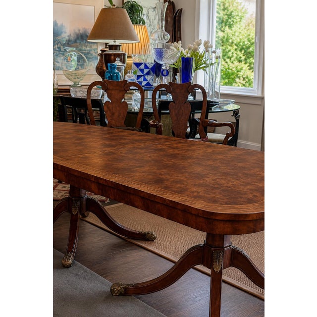 An impressive Regency-style dining table featuring a richly figured burl wood top accented with an elegant brass Greek key...