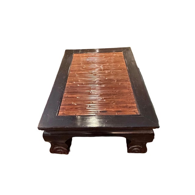 Large low-profile coffee table crafted from solid elm wood with a rich, dark finish. It features an inset slatted rattan...