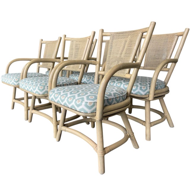 Set of six rattan swivel dining armchairs with cane backs and upholstered seats. Light neutral painted finish with...