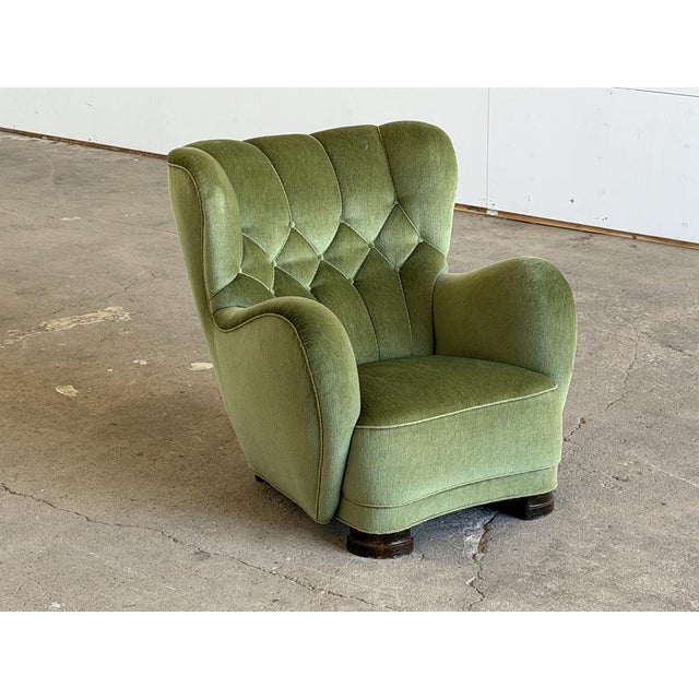 A Danish wingback lounge chair in moss green velvet, circa 1940s. The form is full and generously proportioned — deep...