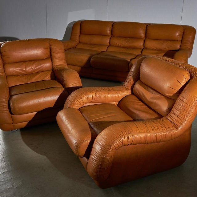 A 3-seater sofa paired with two armchairs in warm brown leather invites relaxation. The seat cushions secure with velcro...