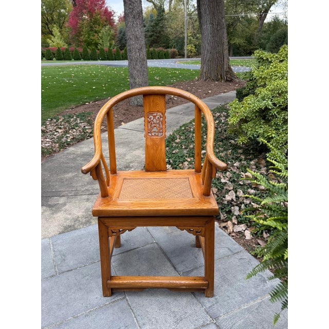 Traditional Chinese horseshoe chair in natural wood features elegant curves, a woven seat, an intricate fretwork carving...