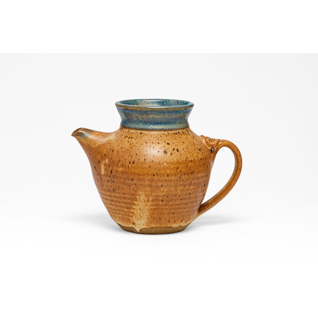 Sculptural pitcher glazed in warm brown hues with muted rim. The handle shows fine incised detail where it joins the body,...