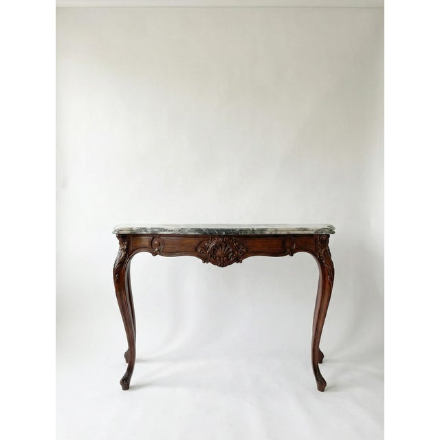 A striking antique French console table in the Louis XV style, this piece features a beautifully carved solid walnut base...