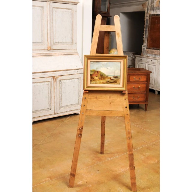 A French 19th century framed oil on panel painting depicting a scene of village life by the sea, under a cloudy sky....