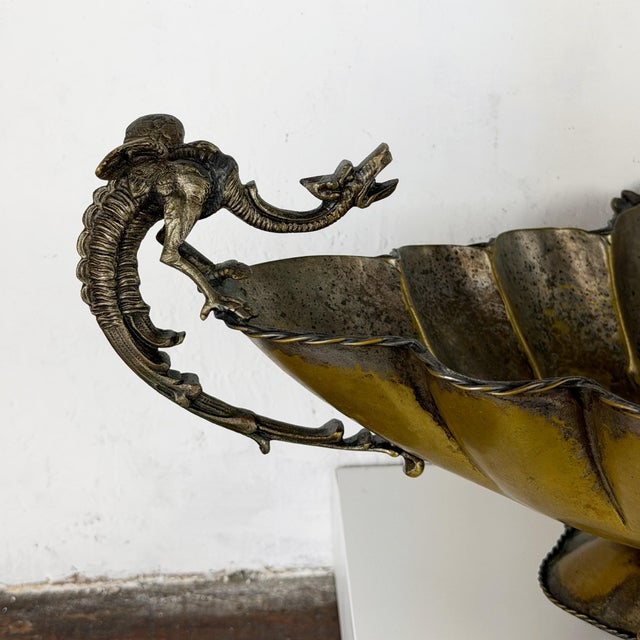 An impressive antique silverplate centerpiece bowl featuring striking dragon handles, ornate shell feet, and decorative...