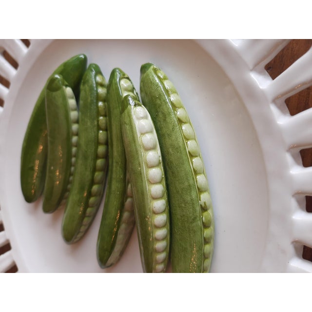 This exquisite Italian ceramic wall plate showcases a delightful design featuring peas nestled in their pods, all set...