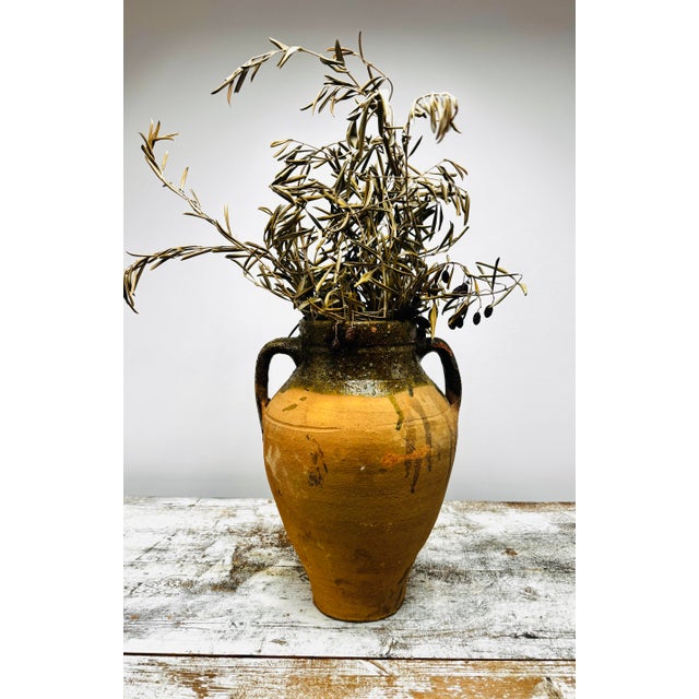 This rustic two-handled olive jar features warm terracotta clay with a rich ochre body and deep olive-green glaze along...