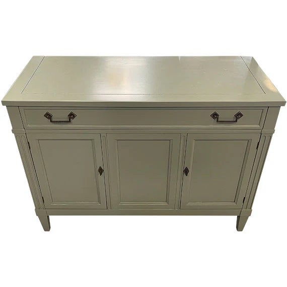 A painted wooden sideboard in a soft sage or muted green finish with a clean, classic silhouette. It features two top...