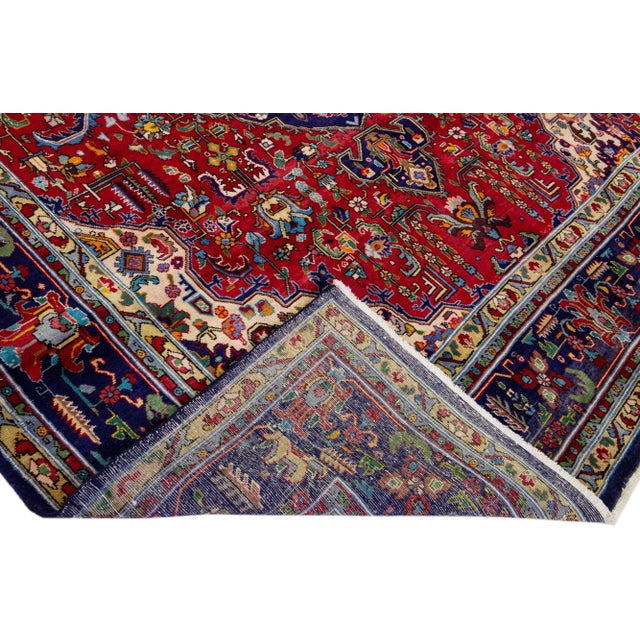 Beautiful vintage Persian Tabriz hand-knotted wool rug with a red color field. This piece has a navy blue frame with...