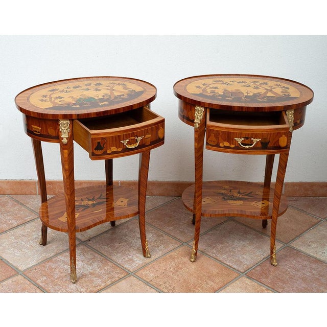 A pair of antique side tables made of fine exotic woods, dating from the early 20th century. The tops are oval in shape...