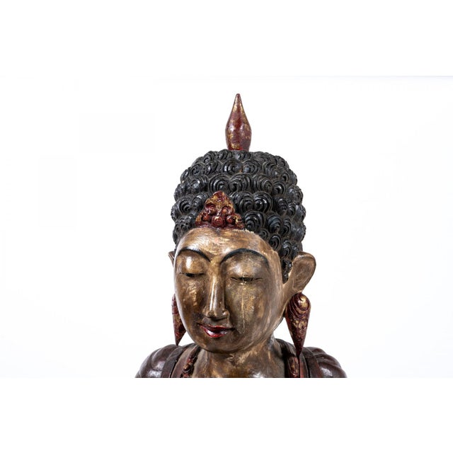 A large carved wooden sculpture of a Buddha in red, black and gilt tones seated in meditation with curled hair, an...