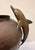 A sculptural brass vessel featuring two gracefully arched dolphin handles positioned symmetrically on either side of the...