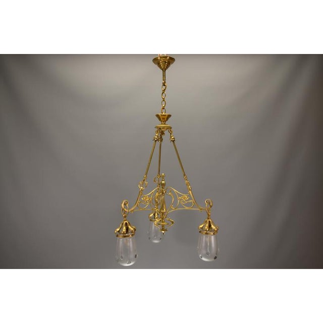 Elegant French Art Nouveau three-light chandelier in brass with frosted glass shades, circa 1920. An elegant French Art...