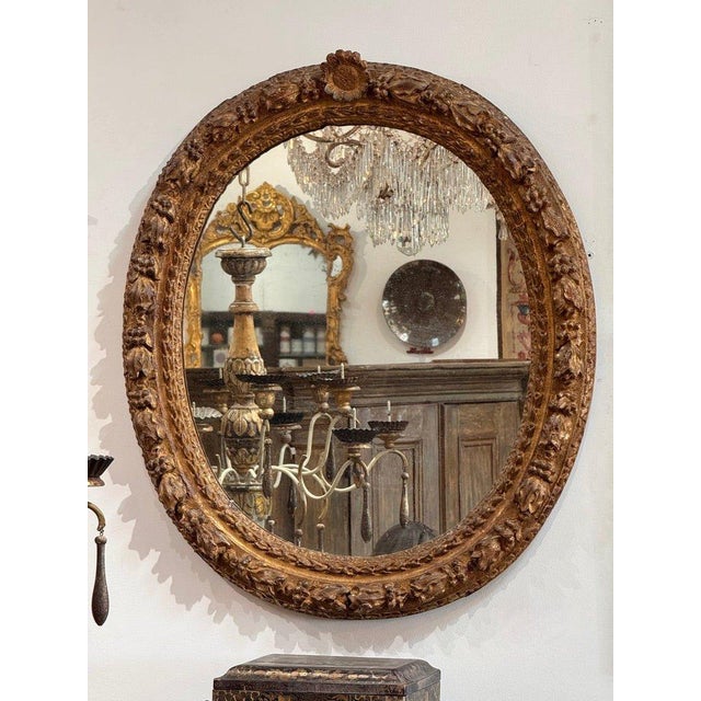 A finely carved Louis XIV period oval mirror, 18th century, retaining its original gilding with rich, time-worn patina....