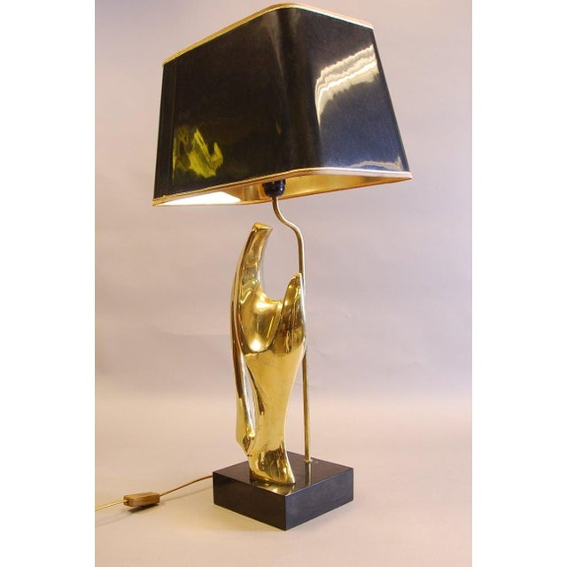 Sculptural table lamp from the 1970s, with a fluid abstract hand-form figure in solid cast brass on a black wood plinth....