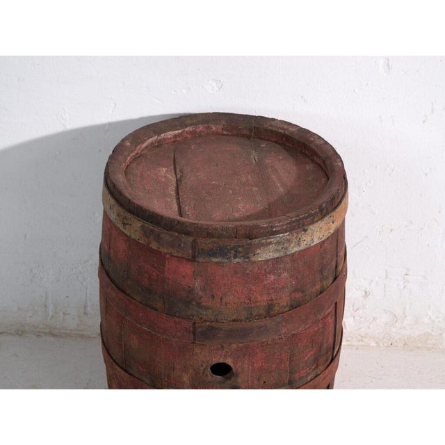 This antique wooden barrel with iron hoops features a cylindrical body of oak staves held by hand-forged iron hoops and...