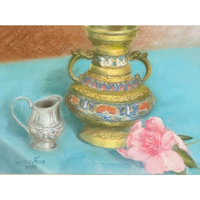 Beautiful painting of still life with a ceramic jar, silver creamer and pink flower over blue tablecloth, signed Audrey...