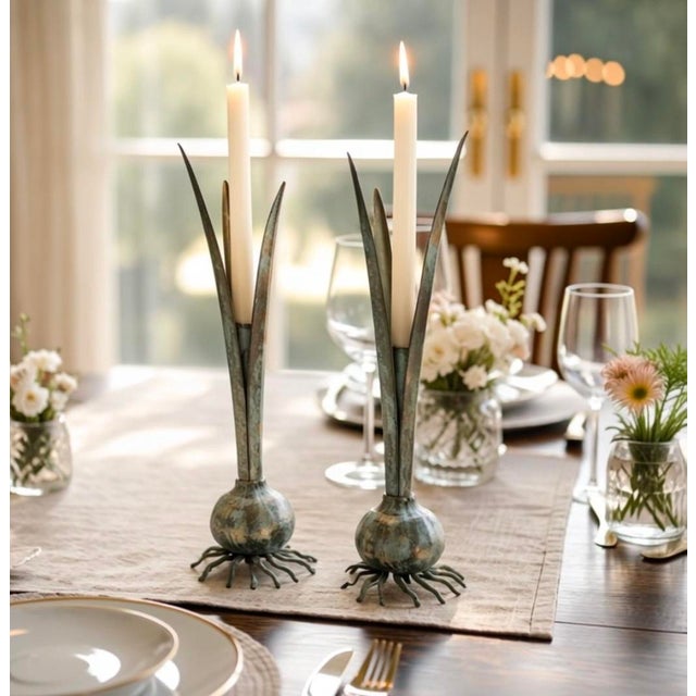 A matched pair of sculptural metal candleholders featuring elongated cattail-and-reed uprights rising from bulbous marine-...