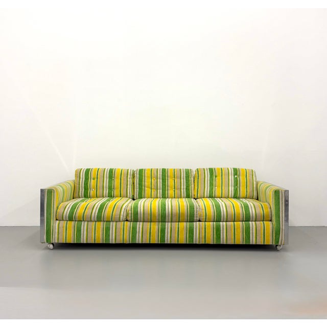 A bold vintage postmodern sofa featuring a polished aluminum frame paired with vibrant striped upholstery in shades of...