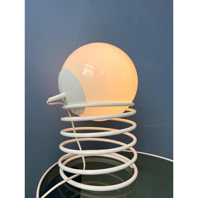 Space age milk glass mid century eyeball table lamp with white metal spiral base. The shade can be placed in the metal...