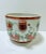A vintage chinoiserie floral cachepot with double handles, soft green ground, rust-toned trim, and hand-painted botanical...