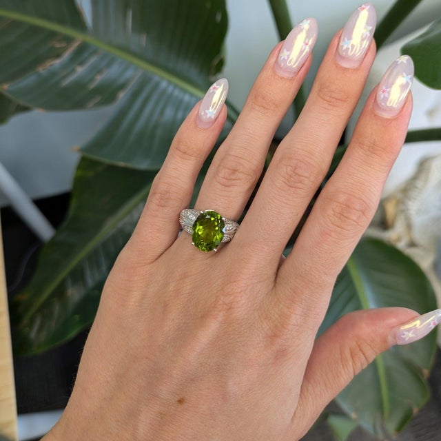 A large natural peridot from Arizona pours fresh lime-green light through this oval ring, encircled by a brilliant halo of...