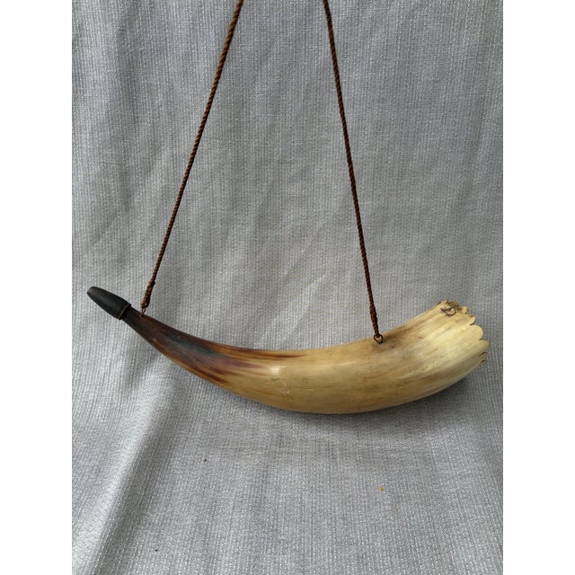 Antique hand made, hollowed cow horn with a woven twisted strap for hanging. Wooden plug on one end, the other a small...