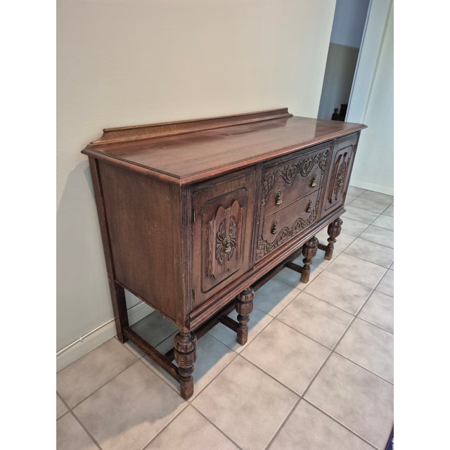 This is a 1920s Jacobean Revival style sideboard crafted from solid oak. Layout: Features two side cabinets flanking two...