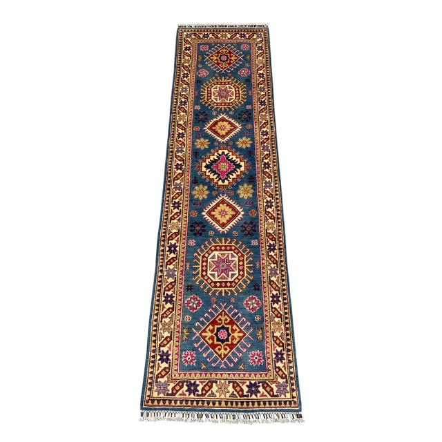 A denim blue field makes the geometric medallions the focal point of this Kazak-style wool runner. Berry pink, burgundy,...