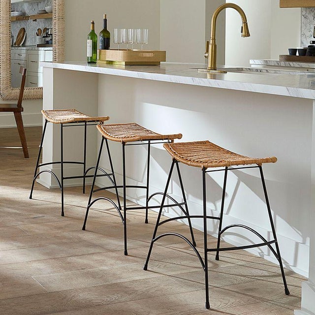 This elegantly arched counter stool offers both comfort and style, featuring a seat wrapped in woven rattan. Its refined...